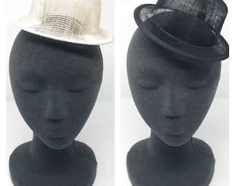 May include: Two small hats on a black mannequin head. The hat on the left is white and the hat on the right is black.