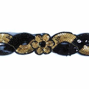 Könnte beinhalten: Ein schwarzes und goldenes Pailletten-Stirnband mit floralem Schmuck. Das Stirnband hat ein sich wiederholendes Muster aus schwarzen und goldenen Pailletten mit einem Blumendesign in der Mitte. Das Design befindet sich auf einem schwarzen Mesh-Träger.