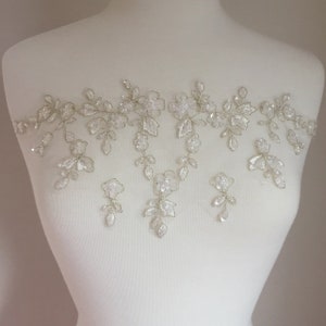 May include: A delicate floral lace applique with clear sequins and gold thread embroidery. The applique features a cascading design with small flowers and leaves.