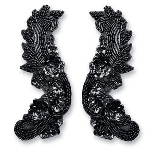 May include: A pair of black beaded embellishments in the shape of a stylized floral design. The embellishments are made of black beads and sequins and have a delicate, intricate design.