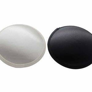 May include: Two bra inserts, one white and one black, are displayed against a white background. The inserts are circular and have a slightly curved shape. The white insert has a textured surface, while the black insert appears smooth.