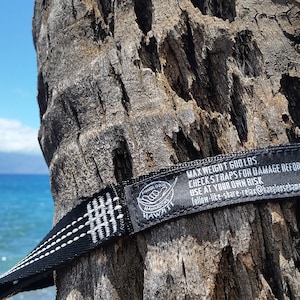May include: Black hammock straps with white stitching and a black label that reads "MAX WEIGHT 600 LBS. CHECK STRAPS FOR DAMAGE BEFORE EACH USE. USE AT YOUR OWN RISK. follow-like-share-relax@hanalenschamnackshawa"