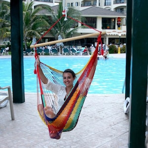 May include: A colorful hammock chair with a red, yellow, and blue striped pattern. The hammock is suspended from a wooden bar and red ropes. The background includes a swimming pool and a resort.