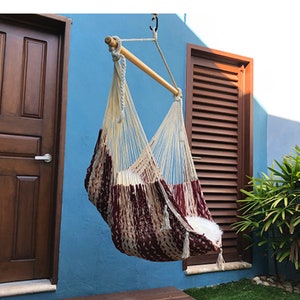 May include: A hanging hammock chair with a brown and white striped pattern. The chair is hanging from a wooden bar and is suspended in front of a blue wall.