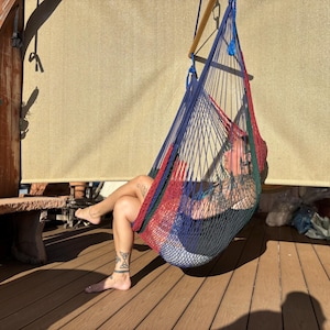 May include: A colorful hammock chair with red, blue, and green woven netting. The hammock is suspended from a wooden structure, offering a relaxing outdoor seating option. The chair is designed for comfort and leisure.