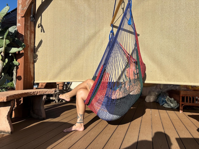 May include: A colorful hammock chair with red, blue, and green woven netting. The hammock is suspended from a wooden structure, offering a relaxing outdoor seating option. The chair is designed for comfort and leisure.