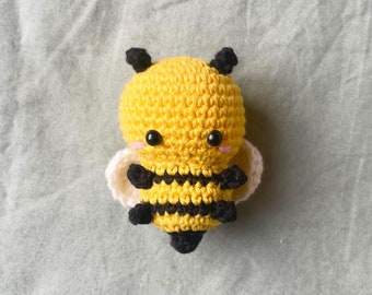May include: A crocheted bee toy with yellow and black stripes, white wings, and black eyes. The bee has a cute, cartoon-like expression.