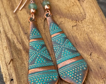 May include: A pair of copper earrings with a turquoise blue and copper patterned design. The earrings have a copper wire hook and a small turquoise blue bead at the top.