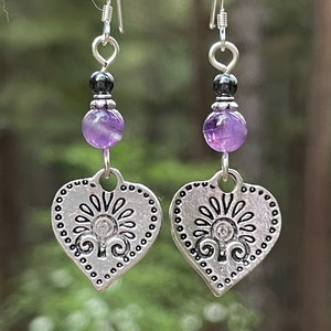 Pode incluir: Brincos de prata em forma de cora&ccedil;&atilde;o com um design floral, com contas de ametista roxa e hematita preta.