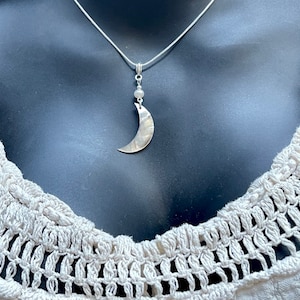 May include: A silver chain necklace with a crescent moon pendant made of mother of pearl. The pendant is attached to a small silver bead.