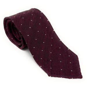 May include: A burgundy tie with a subtle textured appearance and small white polka dots. The tie is rolled up, showcasing its fabric and design. This classic accessory is suitable for formal or business attire.