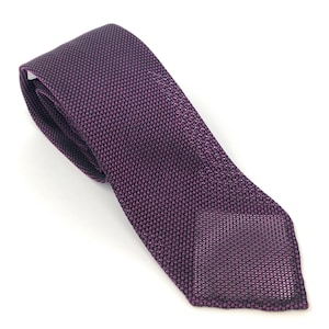 Puede incluir: Una corbata de seda con estampado en negro y morado oscuro. La corbata est&aacute; hecha de un tejido de punto fino y tiene una punta puntiaguda.