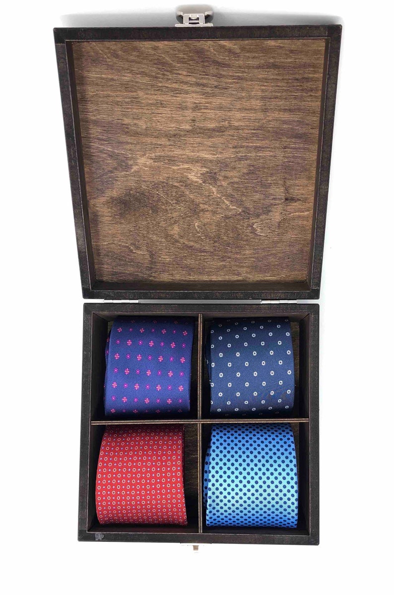 May include: A wooden box with a hinged lid, containing four patterned ties. The ties are arranged in two rows of two, with a blue tie with pink and white pattern, a blue tie with white dots, a red tie with white and yellow dots, and a blue tie with white dots.