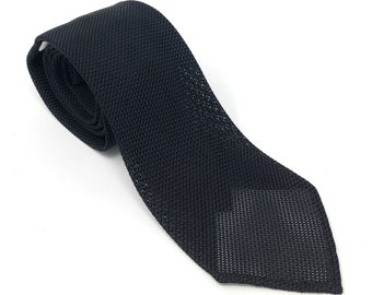 May include: A black knitted tie with a textured pattern. The tie is rolled up and the tip is pointed.