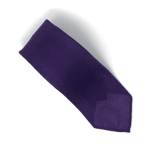 May include: A solid purple necktie with a textured weave. The tie is displayed diagonally against a white background. The tie's color is a deep, rich shade of purple.