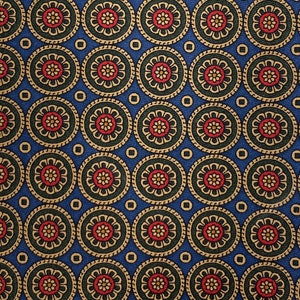 May include: A close-up of a blue fabric with a repeating pattern of circular floral designs. Each circle features a red and yellow flower surrounded by green and gold accents. The background is a solid blue color.