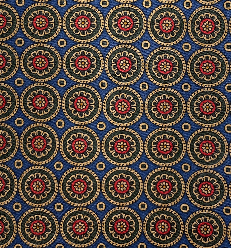 May include: A close-up of a blue fabric with a repeating pattern of circular floral designs. Each circle features a red and yellow flower surrounded by green and gold accents. The background is a solid blue color.