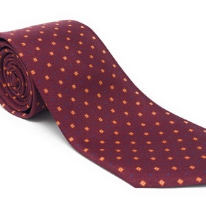 May include: A rolled burgundy tie with a repeating pattern of small orange squares and blue dots. The tie is made of a textured fabric and is displayed on a white background. This classic tie is suitable for formal or business attire.
