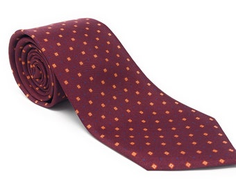 May include: A rolled burgundy tie with a repeating pattern of small orange squares and blue dots. The tie is made of a textured fabric and is displayed on a white background. This classic tie is suitable for formal or business attire.