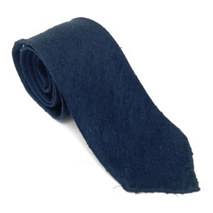 May include: A navy blue tie with a textured, slightly rough surface. The tie is rolled up, showing the fabric's detail and color. The tie is a classic accessory for formal or business attire.