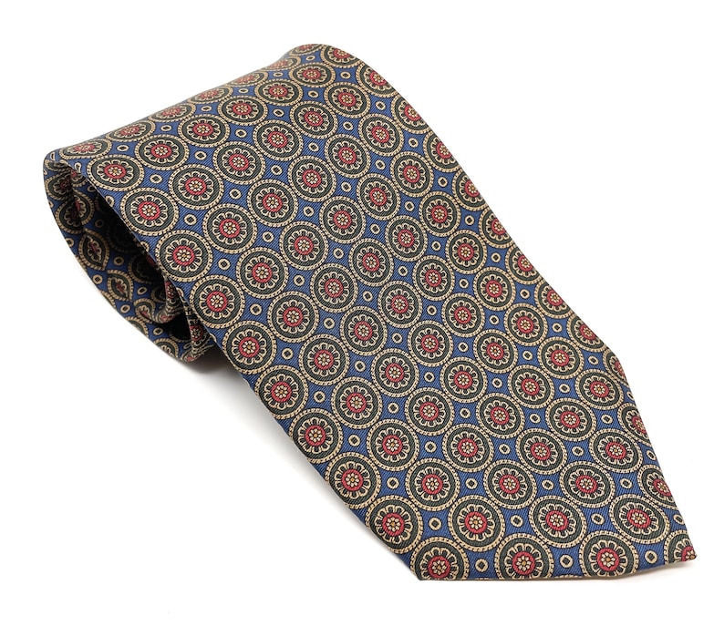 May include: A patterned necktie featuring a repeating floral design in red, tan, and green on a blue background. The tie is rolled up, showcasing the intricate pattern and fabric texture. A classic accessory for formal or business attire.