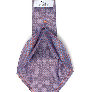 May include: A blue and red patterned tie with the brand name "WILMOK ROME" on a white label. The tie features a repeating geometric design in shades of blue and red. The tie is displayed against a white background.