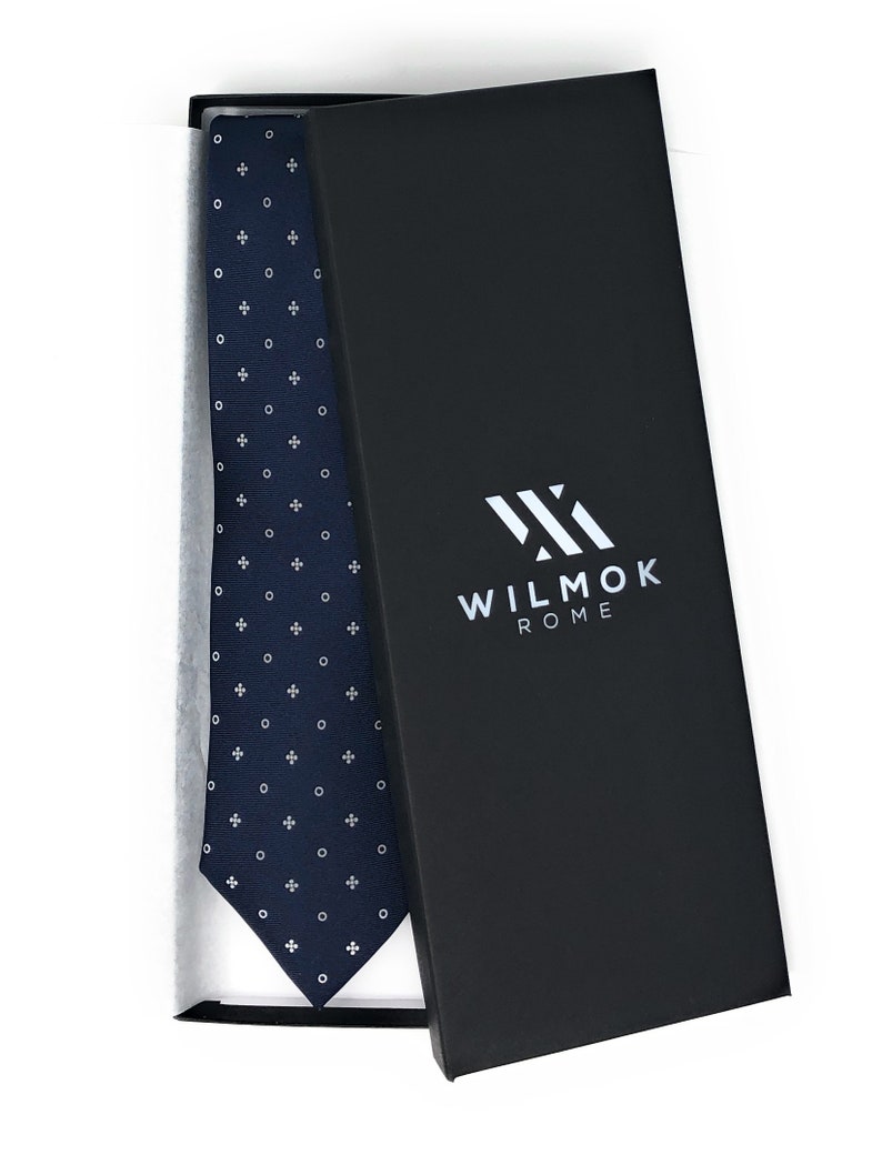 May include: A navy blue tie with a white pattern of circles and crosses in a box with the text "WILMOK ROME" on the box.