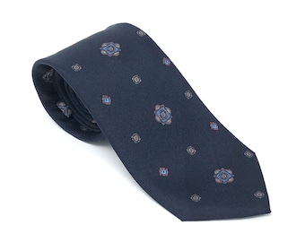 May include: A dark blue patterned tie with a repeating geometric design in shades of blue, red, and brown.