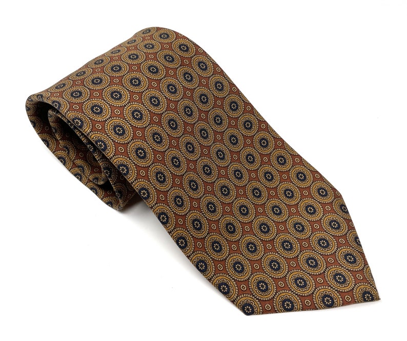 May include: A brown tie with a repeating circular pattern in gold and navy blue. The tie is made of a smooth fabric and is neatly folded, showcasing the intricate design. The tie is a classic accessory.
