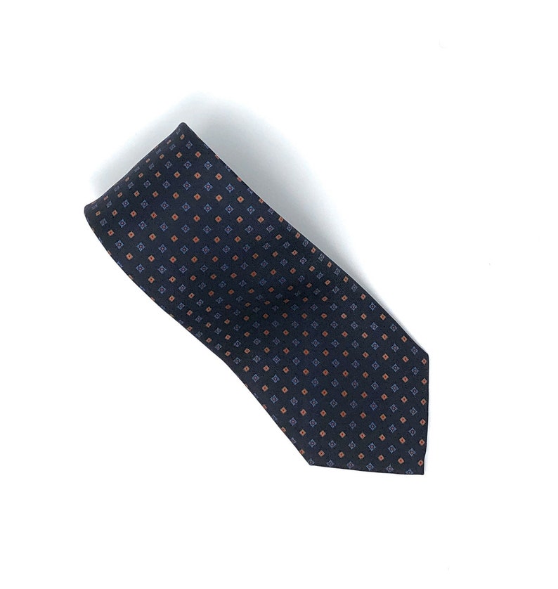 May include: A dark blue necktie with a repeating pattern of small orange and blue squares.