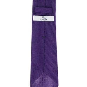 May include: A solid purple tie with a textured knit pattern. The tie features a label with the text "WILMOK ROME" in white. The tie is a classic accessory for formal or business attire.