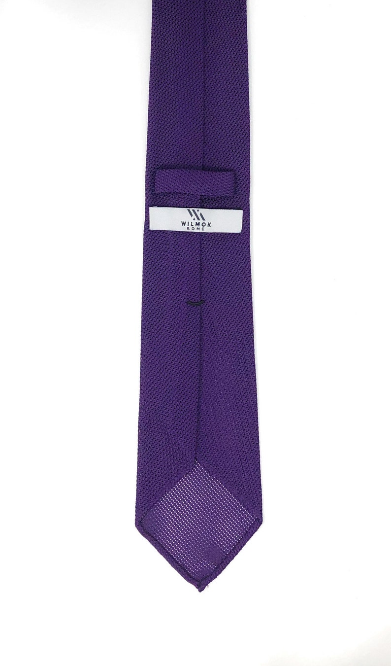 May include: A solid purple tie with a textured knit pattern. The tie features a label with the text "WILMOK ROME" in white. The tie is a classic accessory for formal or business attire.