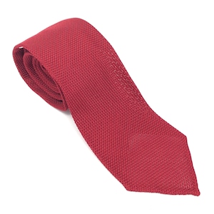 Puede incluir: Una corbata roja de punto, dispuesta en diagonal sobre un fondo blanco. La corbata, con su textura visible, es un accesorio clásico para vestimenta formal o de negocios.