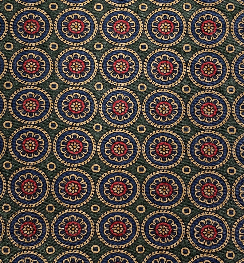 May include: Close-up of a patterned fabric with a repeating circular design. Each circle features a red floral center, surrounded by blue and gold detailing, set against a dark green background. Small gold squares are interspersed between the circles.
