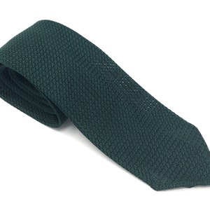 Puede incluir: Una corbata de punto verde oscuro, sobre un fondo blanco. La corbata tiene una textura y un patrón sutil. Un accesorio clásico para vestimenta formal o de negocios.