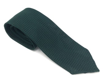 May include: A dark green knitted tie, angled across a white background. The tie is made of a textured fabric, with a subtle pattern visible. The tie is a classic accessory for formal or business attire.