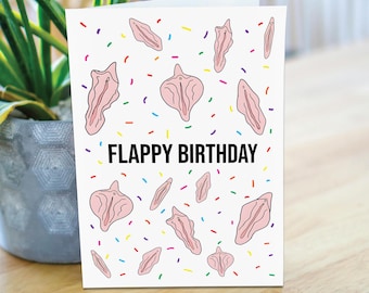 May include: A white greeting card with the text "FLAPPY BIRTHDAY" in black. The card features a pattern of pink illustrations and colorful confetti. The card is displayed on a wooden surface with a potted plant in the background.