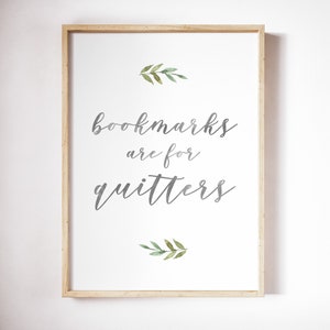 May include: A framed print with a white background and gray text that reads "bookmarks are for quitters". The text is in a cursive font. There are two small green watercolor leaf sprigs above and below the text.