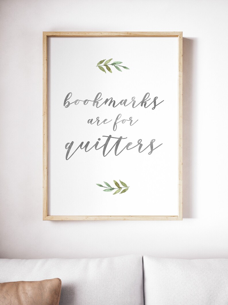 May include: A framed print with a white background and gray text that reads "bookmarks are for quitters". The text is in a cursive font. There are two small green watercolor leaf sprigs above and below the text.