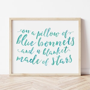 Pode incluir: Impressão emoldurada com a frase "on a pillow of blue bonnets and a blanket made of stars" em escrita turquesa. A moldura é de madeira clara, sobre um fundo branco.