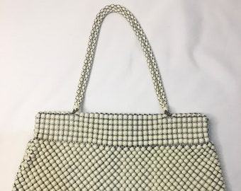 May include: A white beaded handbag with a chain strap. The bag is made of small, round beads that are woven together to create a mesh-like pattern.