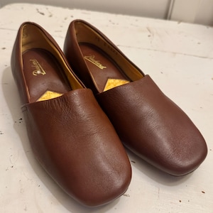 May include: A pair of brown leather slip-on shoes. The shoes have a rounded toe and a low heel. The interior is lined with a yellow material. The brand name "Packard" is visible inside the shoe.