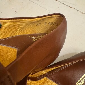 May include: Close-up of a pair of brown leather shoes. The interior lining is yellow. The shoes have the brand name "Packard" printed on the insole. The size is marked as "7.5 D 4223".
