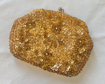 May include: A gold sequined evening bag with a floral design. The bag is made of a soft fabric and has a clasp closure.