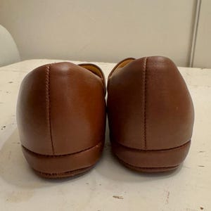 May include: A pair of brown leather loafers. The shoes are displayed from the back, showcasing the rounded heels and stitched seams. The leather has a smooth, polished appearance.