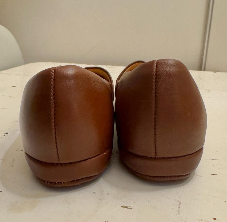 May include: A pair of brown leather loafers. The shoes are displayed from the back, showcasing the rounded heels and stitched seams. The leather has a smooth, polished appearance.