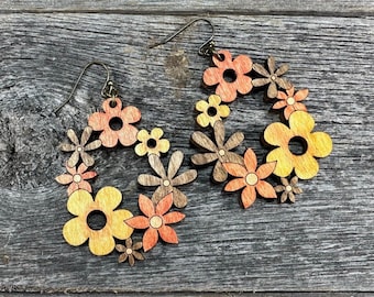 May include: Wooden flower earrings with a teardrop shape. The earrings feature a variety of flower sizes and colors, including orange, yellow, and brown. The earrings have a bronze-colored hook.