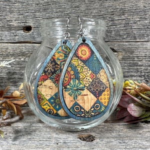 Könnte beinhalten: Ein Paar tropfenförmige Ohrringe mit einem blauen und mehrfarbigen Muster. Die Ohrringe sind aus Holz und haben silberne Haken.