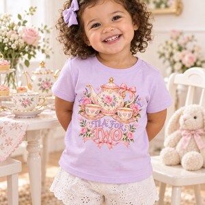 Puede incluir: Una camiseta de manga corta de color morado claro con un estampado gráfico de una tetera floral y dos tazas de té con el texto "TEA FOR TWO" en letras rosas y doradas, combinada con pantalones cortos blancos de encaje.