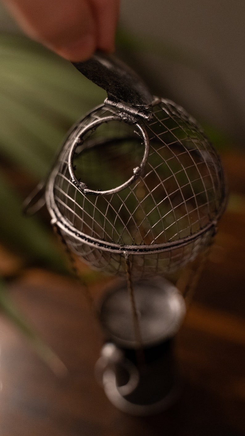 May include: A silver metal hot air balloon candle holder with a wire mesh design. The balloon is open at the top and has a small candle inside.